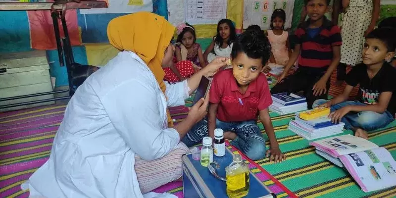 A doctor is checking the ears of a young Rohingya child in their classroom