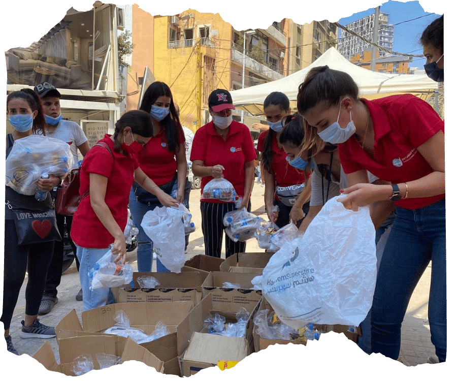 Food distribution in Lebanon - a group of staff from our partner orgnanisation wearing red tshirts are filling bags with bottled water and other supplies to make up relief packs for families in need. 