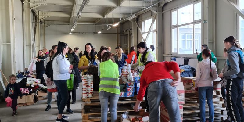 Transit centre for refugees with volunteers handing out supplies in a warehouse building