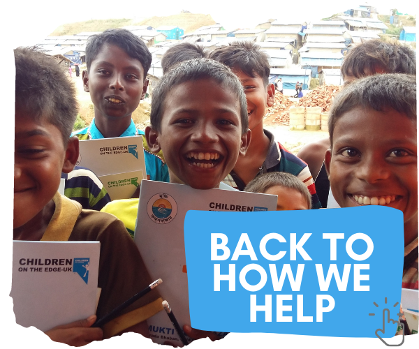 You can click this image to go back to the main 'How we help' page. The image shows Rohingya refugee boys with Children on the Edge text books smiling and laughing at the camera. Behind them is a steep hill full of makeshift shelters. 
