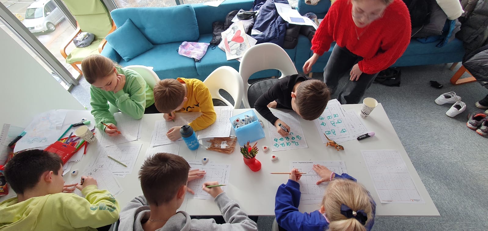 6 children pictured from above doing drawing and activities at a white table