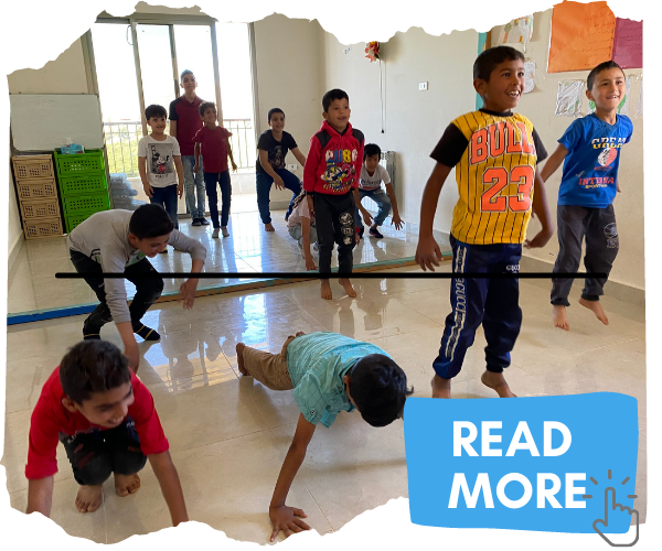 Group of Syrian refugee boys doing a exercise class, jumping up and down and crouching. Attached button image invites you to click to read more. 