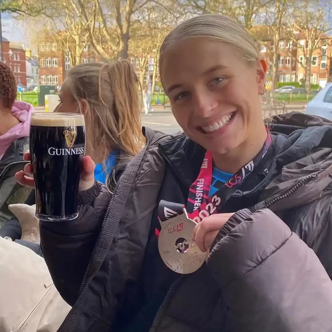Lizzie holding her medal and a pint after completing the London Marathon 
