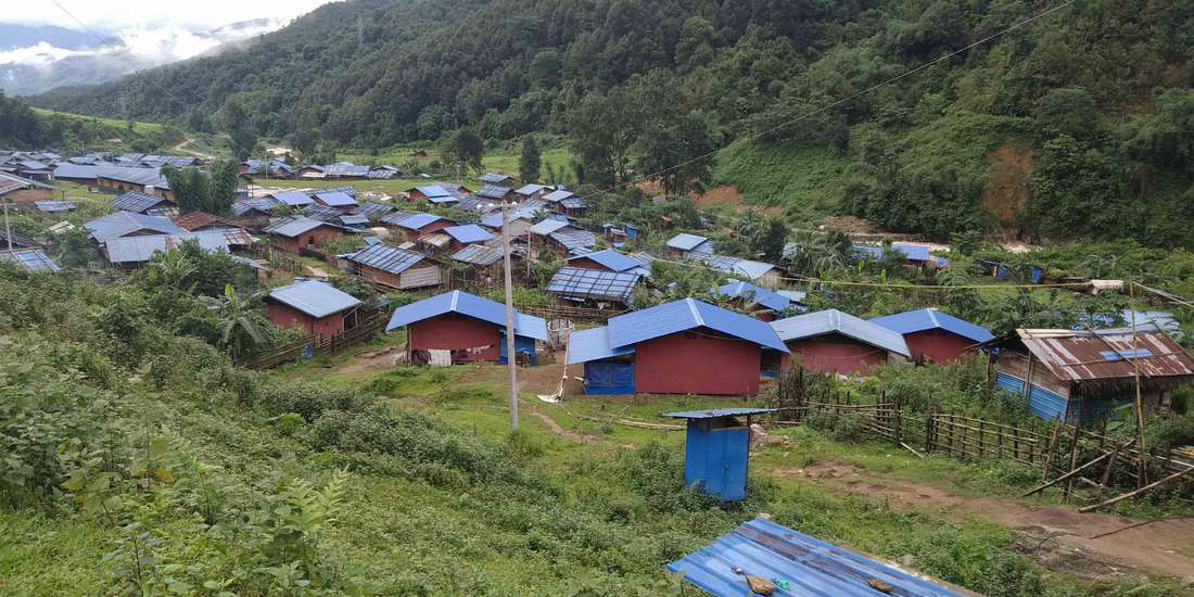 Displacement camp set in the mountains of Kachin State Burma. Around sixty shelters with blue roofs situated in a mountain ridge that is full of trees. The mist on the top of the mountain is viewable in the background. 