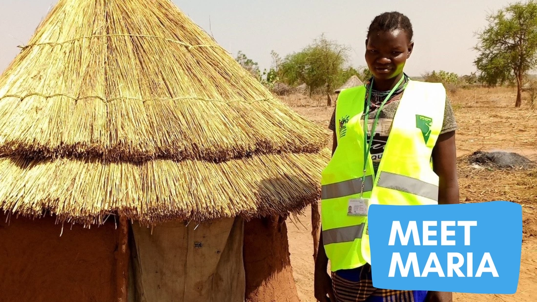 Meet Child Protection Team Member Maria. Maria standing next to a small hut