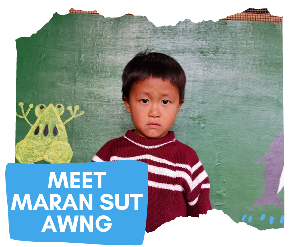 Superimposed words on this image read 'Meet Maran Sut Awng' and image shows a four year old boy from Kachin State Myanmar with a dark red jumper, stood in front of a mural and looking directly at the camera. 