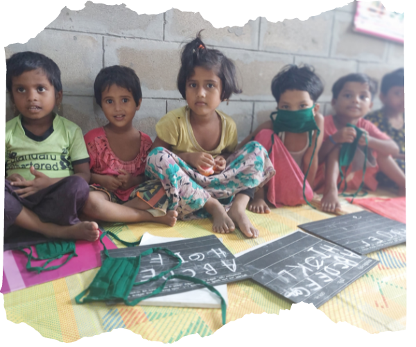 Younger Rohingya refugee children sat on a yellow mat in a new classroom building with chalkboards in front of them.