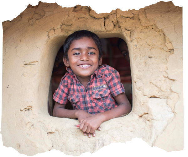 Rohingya boy looks out of the window of a mud shelter in Kutupalong camp and smiles at the camera. He is wearing a red and blue checked shirt. 