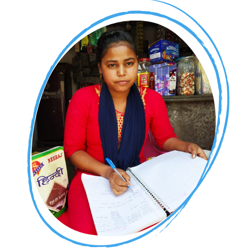 Poonam, a 17 year old Dalit teen is wearing a red dress with a navy blue scarf and is writing in a notepad in front of her small shop front in India.