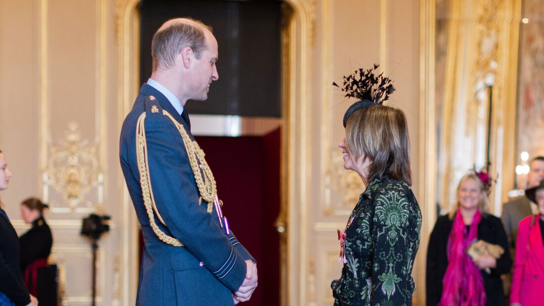 Prince William and Rachel Bentley smiling in conversation at OBE award ceremony.