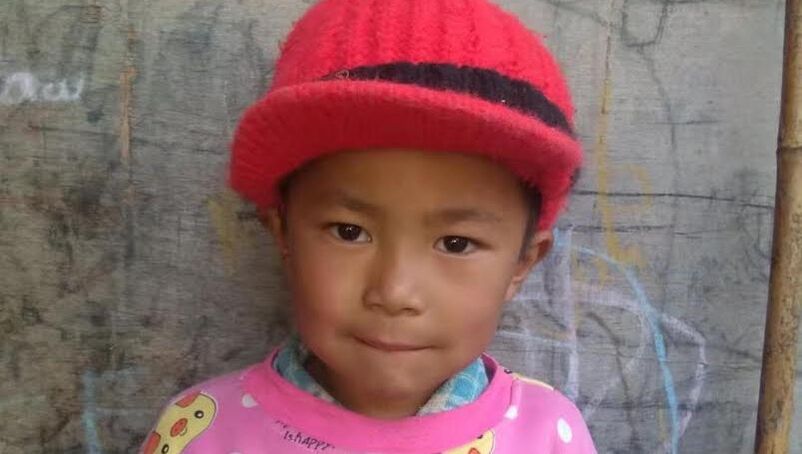 4 year old Shari Bawk Awng Mu Hpa is wearing a red hat and pink jumper