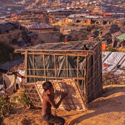 Rohingya boy carries a bamboo structure against backdrop of vast refugee camp