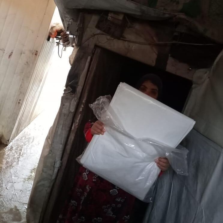A Syrian refugee woman receiving a new tarpaulin at the doorway of her tented home