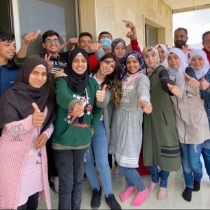 A group of Grade 9 Syrian refugee students in Lebanon celebrating their exam success. A group photo on their school balcony, everyone is smiling with their thumbs up.