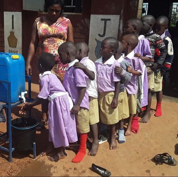 Ugandan preschoolers wearing purple school uniform queuing up outside their school building to wash their hands 