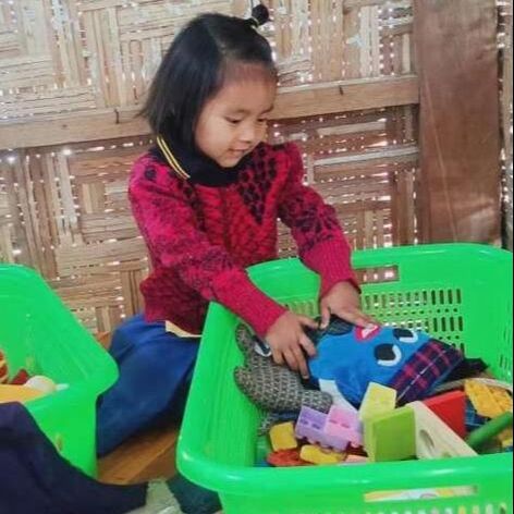Kawn Ja Htoi Tsin reaching into a toy basket full of colourful blocks 