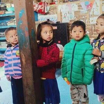 Four young Kachin children stood inside their preschool classroom, in the middle is Kawn Ja Htoi Tsin