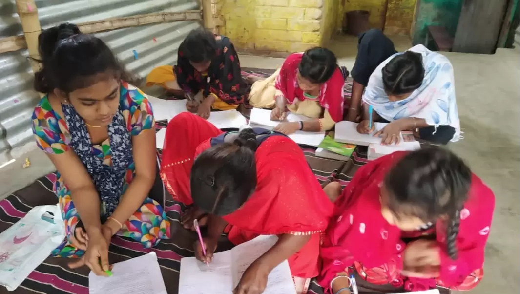 6 teenage girls in India are sat on a mat writing in their notebooks