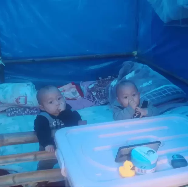 Two babies in makeshift cot bed in a blue temporary shelter