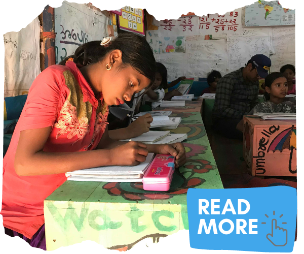 Young Rohingya refugee girl sat at a colourful desk doing her classwork. You  can click on the image to read more about how we educate refugee children. 