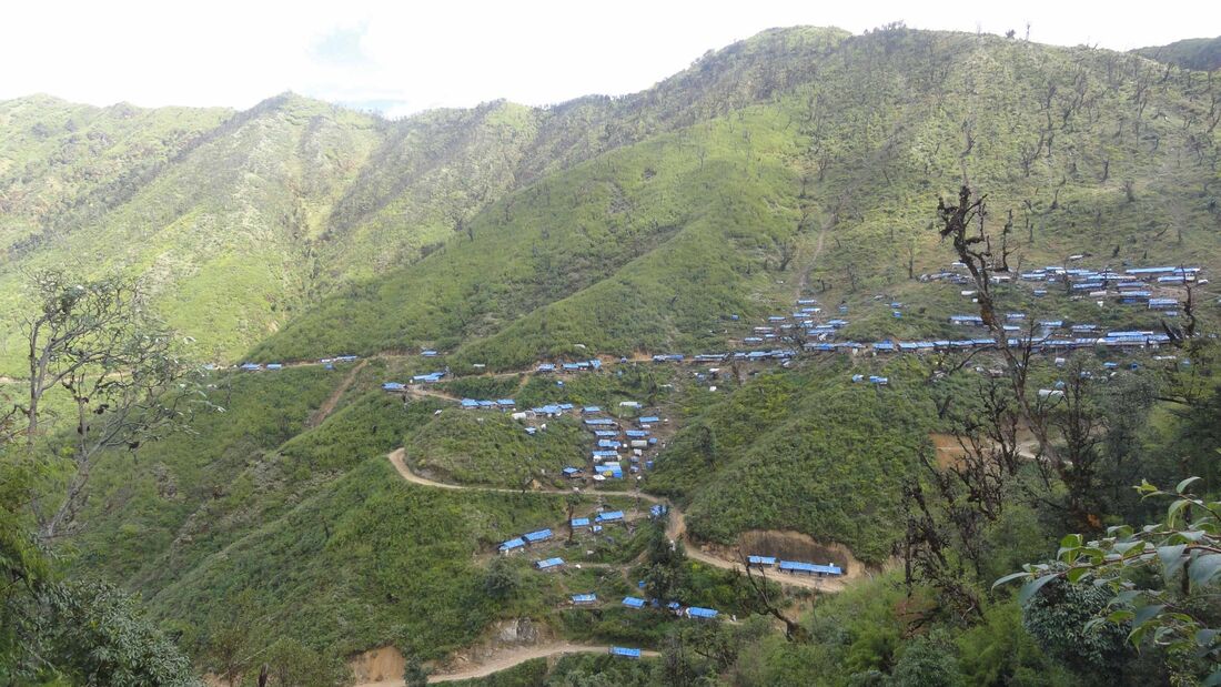 Remote mountain camps in Kachin State, Myamar - photo shows lines of huts with blue roofs in a huge green mountain vista