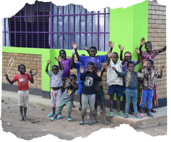 Group of Congolese refugee children aged between 4 - 10 standing outside a learning centre smiling and waving. 
