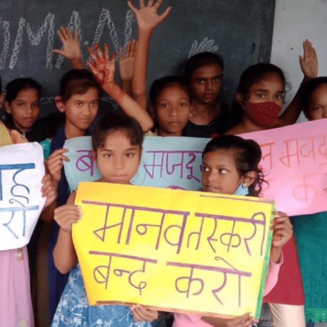 Group of Indian school children gathered together in front of a chalk board holding up coloured signs and smiling. They are happy to be back at school in India after lockdown. You can click on the image to read more in a blog post.