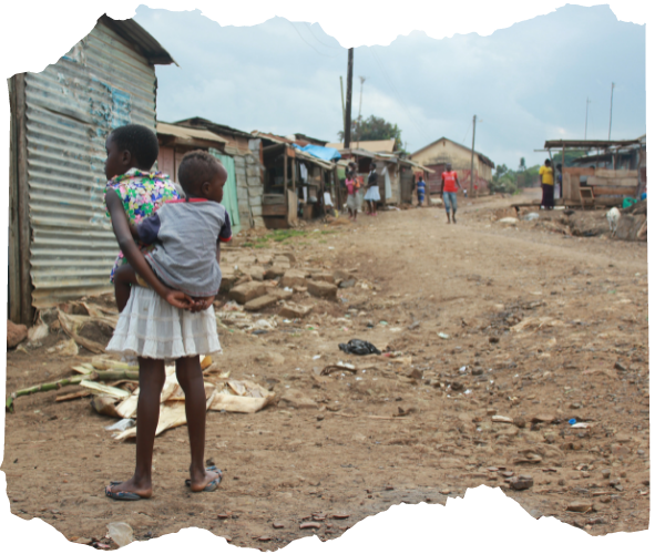 Ugandan child carries baby on her back, standing in a Ugandan slum with corrugated iron huts and rubbish on the dirt floor. 