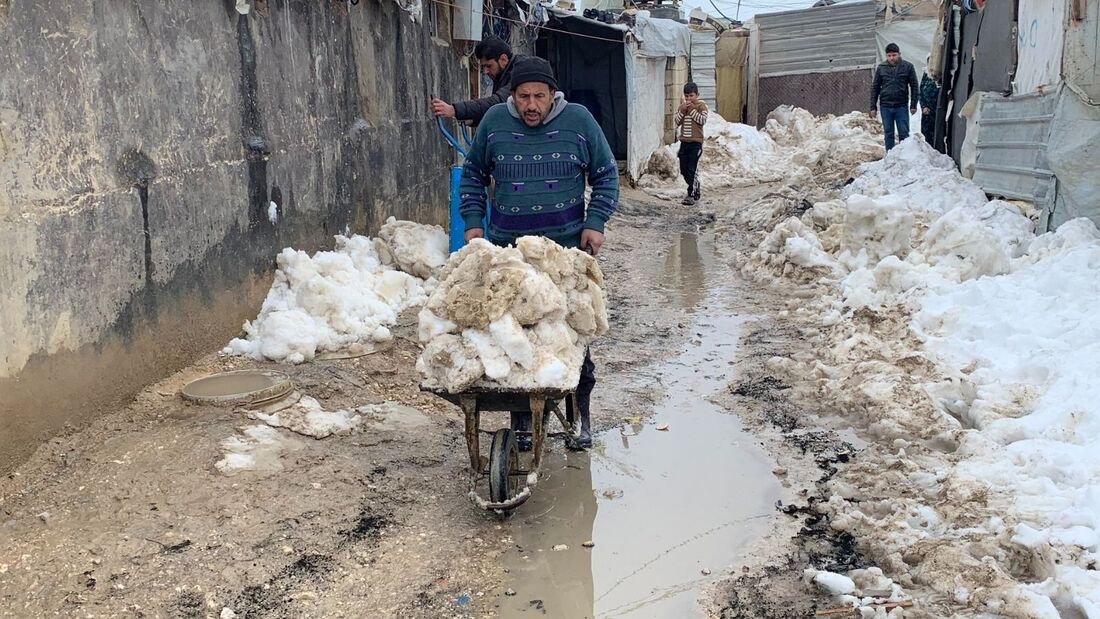 A Syrian refugee man is pushing a wheelbarrow of snow through to clear a path between canvas shelters in a refugee camp in Lebanon