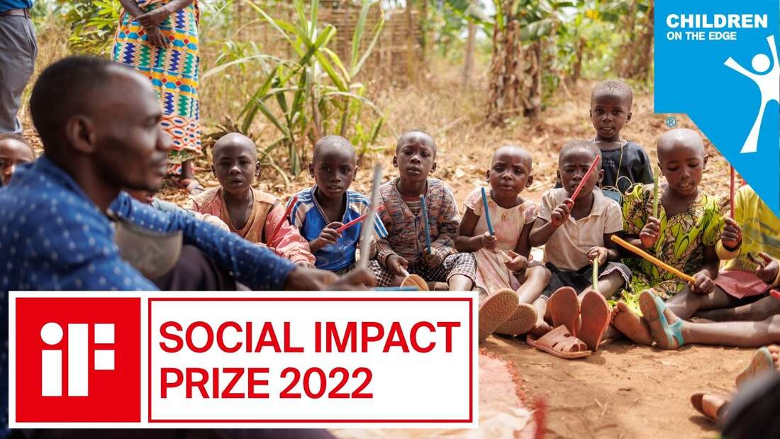 A group of Congolese refugee children are sat outside in front of some trees with a male teacher. They are holding coloured sticks and looking at him. The image has the iF design logo and the text: 'Social Impact prize 2022'