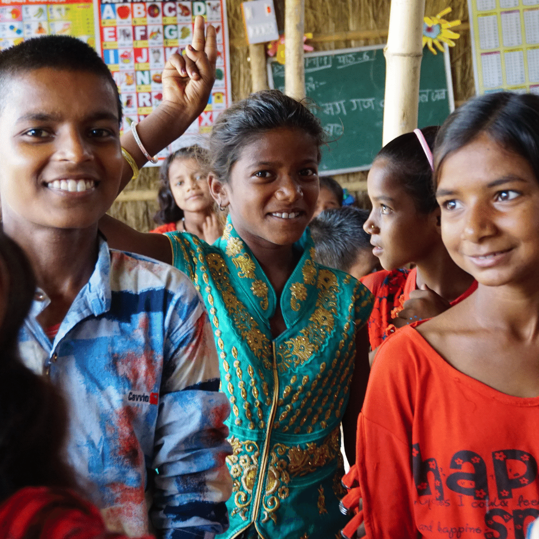 A classroom full of Indian children. The three children at the front of the image are facing the camera and smiling. They are wearing bright coloured clothes. You can click on the image to read the blog post.  