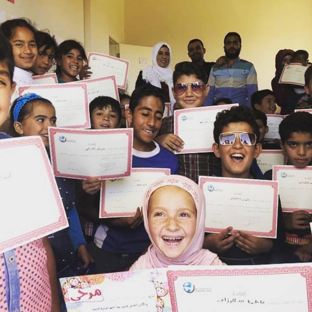 A group of 17 Syrian students who are close together and holding up their graduation certificates. They are all smiling. Three adult teachers are standing behind the students. You can click this image to read a story about the children heading back to school after lockdown in Lebanon.