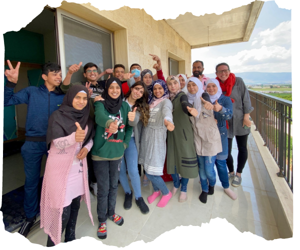 A group of Syrian teens are stood on the balcony of their school smiling with their thumbs up