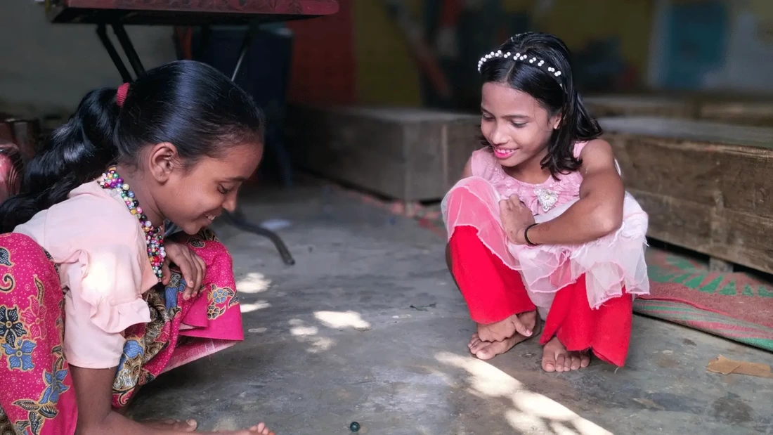 Tosmin a young Rohingya girl and her friend are playing marbles on the floor