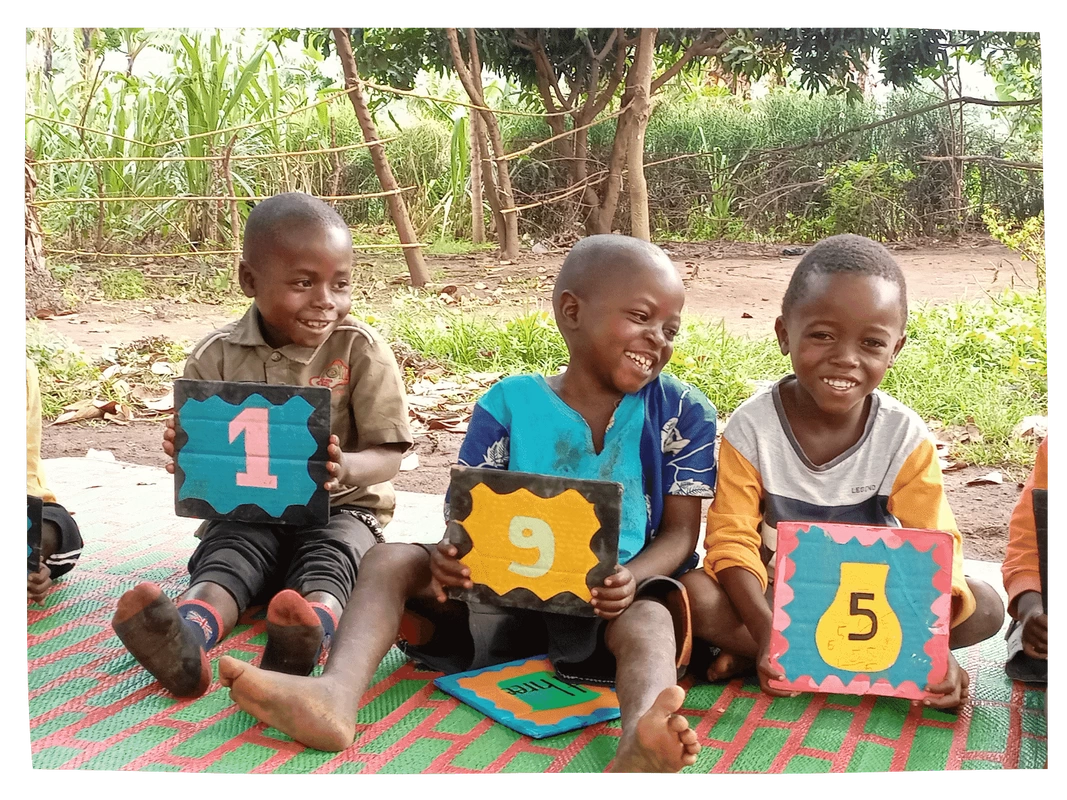 Three young Congolese children learning outside smiling