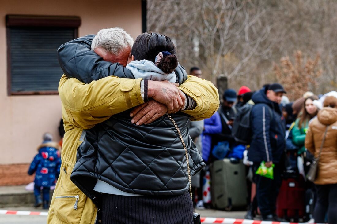 Two Ukrainian refugees hugging in front of a queue of refugees