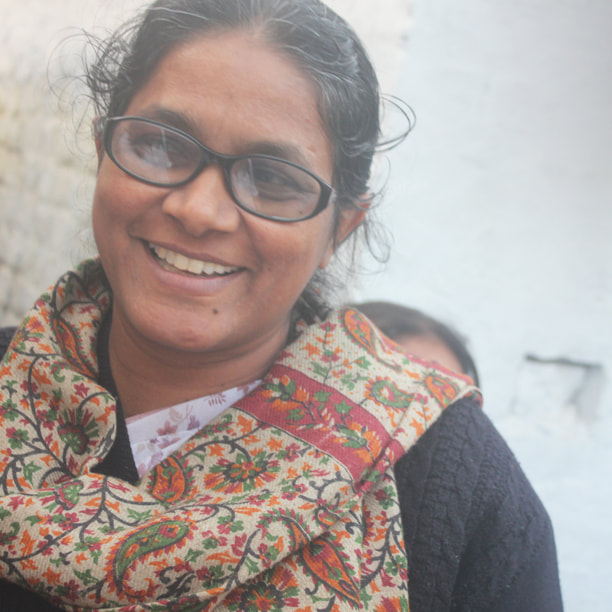 Veena, an Indian woman with dark hair and glasses is smiling at the camera